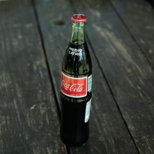 A classic Coca-Cola bottle placed on a rustic wooden table outdoors.